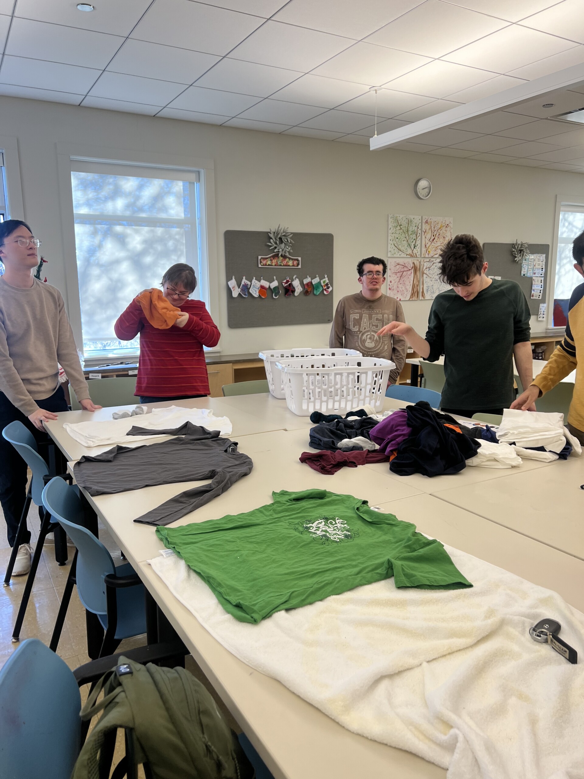 Group of Catalyst members, one woman and two men, holding clothes and laundry on a table, focused on folding tasks inside the CEL building.