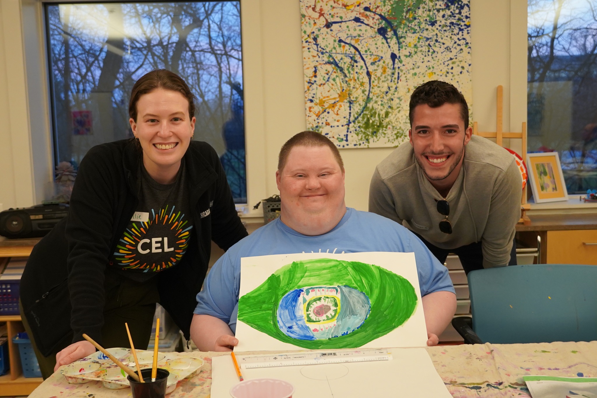 A group photo of two Young Leadership Committee members and CEL members smiling, with one member proudly holding artwork.